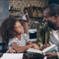 A father and daughter sitting together and reading a book.